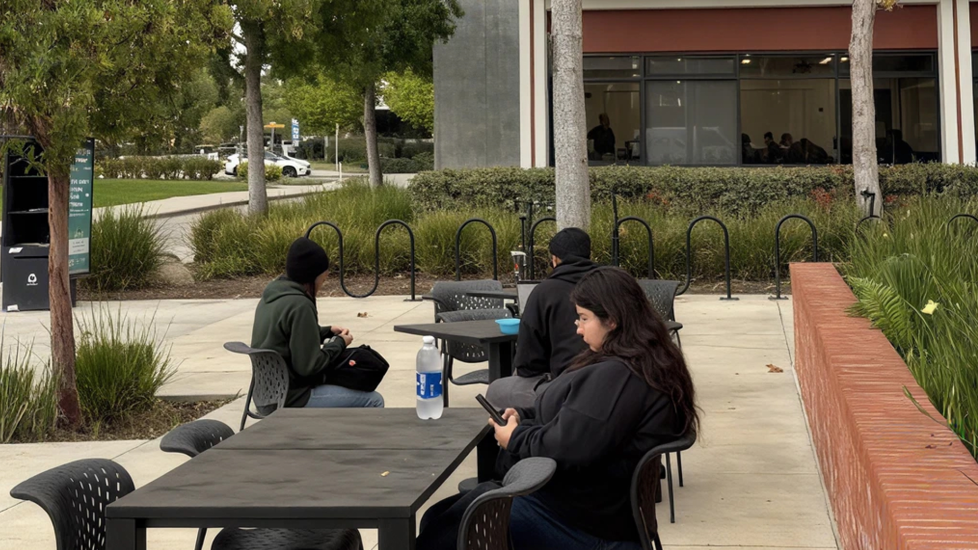A student sitting alone in a campus space, headphones in, looking at a phone